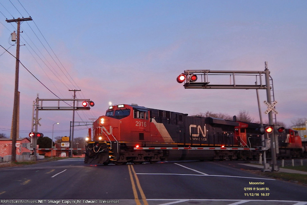 Q199 rolls beneath the moon across Scott St. into Shops at dusk